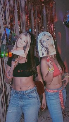 two young women standing next to each other in front of a wall with pictures on it