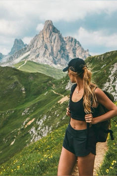 a woman standing on top of a lush green hillside next to a tall mountain range