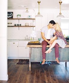 a man and woman sitting on top of a kitchen counter