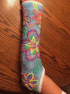 someone's foot with colorful flowers and butterflies painted on it, next to a wooden table