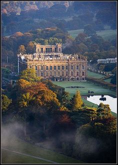 an aerial view of a large building in the middle of trees with fog around it