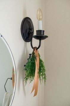 a candle is lit on the wall next to a mirror with a ribbon around it