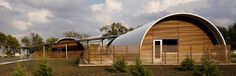 an unusual wooden building sits in the middle of a field with trees and bushes around it