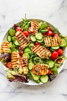 grilled chicken and cucumber salad in a white bowl on a marble table