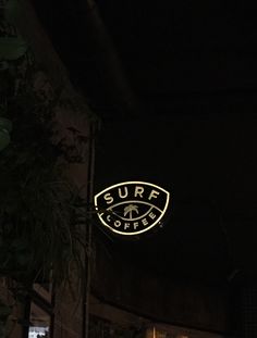 the surf coffee sign is lit up in the dark sky above some bushes and trees