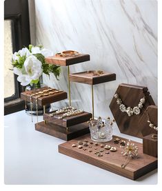 several pieces of jewelry are on display in front of a marble wall and vase with white flowers