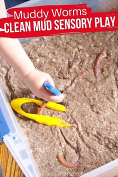 a close up of a child's hand holding scissors in front of muddy worms