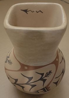 a white vase sitting on top of a table next to a black and red object