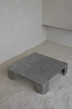 a concrete coffee table sitting on top of a white sheet covered floor in an empty room