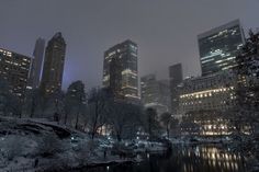 the city is lit up at night with snow on the ground and trees in the foreground