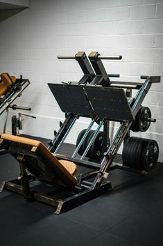 an empty gym room with weight machines and barbells on the floor in front of a white brick wall