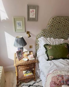 a bed sitting next to a table with two lamps on it and pictures above it