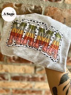 a person holding up a t - shirt with the word mama on it in front of a brick wall