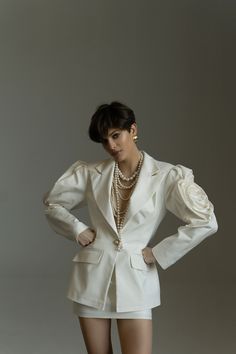 a woman in short shorts and a white jacket with pearls on her neck, posing for the camera