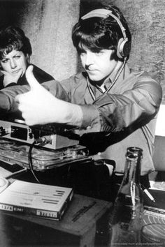 two young men sitting at a table with headphones on and pointing to the radio