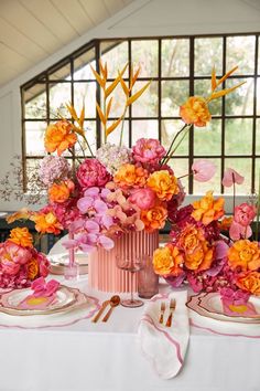 the table is set with pink and orange flowers in vases, plates and napkins