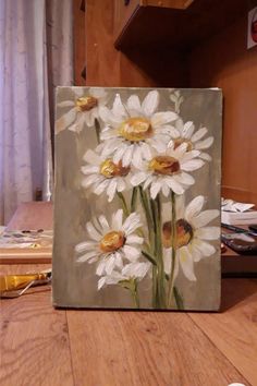 a painting of white daisies on a wooden table