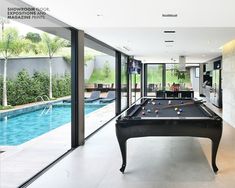 a pool table in the middle of a living room with large windows and sliding glass doors