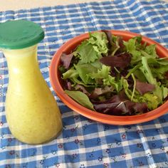 a salad in a bowl next to an apple on a checkered tablecloth with a green shaker