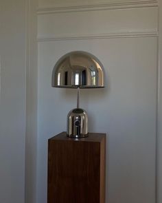 a chrome lamp on top of a wooden block in a room with white walls and wood flooring