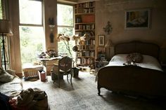 a bedroom with a bed, desk and chair in it's center area next to a large window