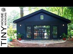 a small black building with glass doors in the middle of trees and bushes around it