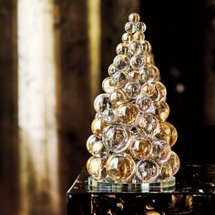 a glass christmas tree sitting on top of a black table next to a mirror wall