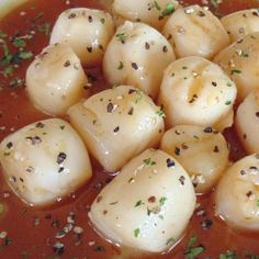 some dumplings are in a red sauce with parsley on the top and green garnish