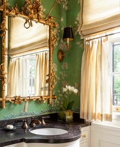 a bathroom with green walls and floral wallpaper, gold mirror over the sink and black marble countertop