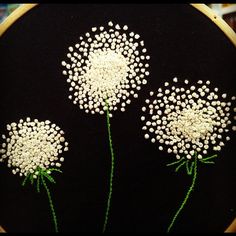 three white flowers are in the middle of a black embroidery hoop with beads on it