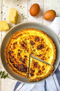 a quiche with one slice cut out on a plate next to eggs and butter