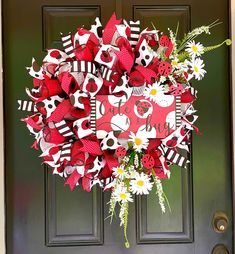 a red and white wreath with ladybugs, daisies and flowers on the front door