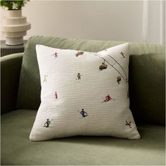 a white pillow with skiers on it sitting on a green couch next to a plant