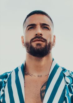 a man with tattoos on his chest wearing a blue and white striped shirt looking up at the sky