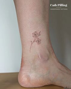 a small flower tattoo on the foot of a woman's left leg, which is sitting on top of a wooden table