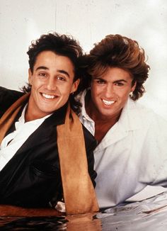 two men are smiling and posing for a photo with one holding a brown scarf around his neck