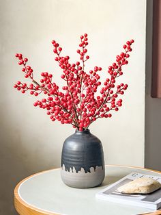 a vase with some red berries in it sitting on a table next to a book