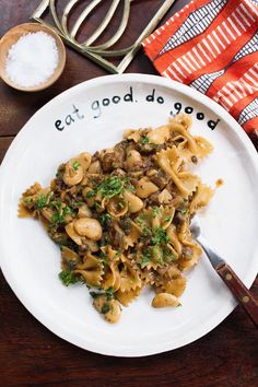 a white plate topped with pasta covered in mushrooms and parsley next to utensils