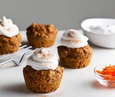 carrot muffins with whipped cream on top sitting on a cooling rack next to small bowls