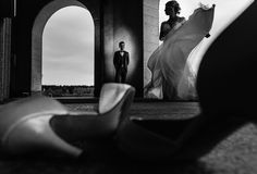 black and white photo of bride and groom in front of arch with shoes on the ground