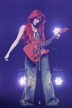 a woman with long red hair playing an electric guitar