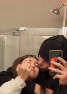 two people taking a selfie in front of a mirror with one person holding a cell phone