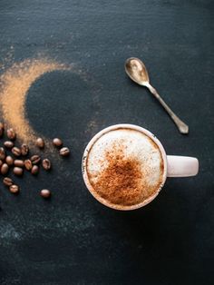 a cappuccino with cinnamon sprinkles and coffee beans next to it