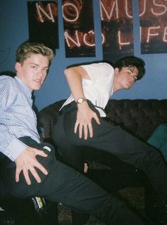 two young men sitting on a couch with their arms around each other's legs