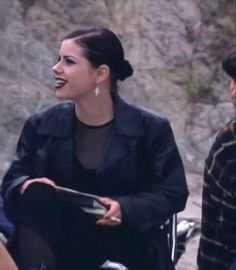 a woman sitting on top of a chair next to a man in a black jacket