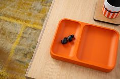 an orange tray with two black beads on it next to a coffee cup and cell phone