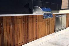 an outdoor bbq grill with wooden cabinets and stainless steel ovens on the side