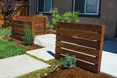 a wooden fence in front of a house with grass and flowers growing on the ground