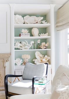 a white chair sitting in front of a book shelf filled with books and vases