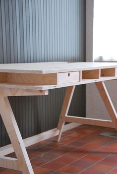 a wooden desk sitting on top of a red tile floor next to a gray wall